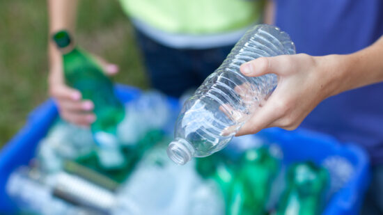 Hands placing bottles in recycling bin
